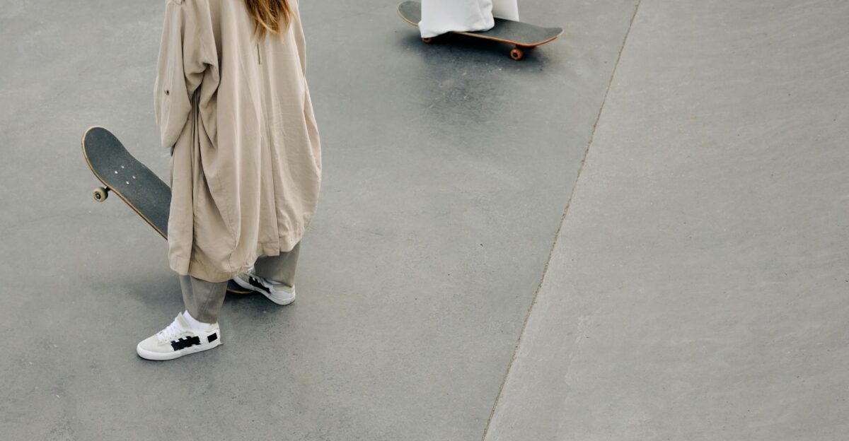 Two individuals in trench coats with skateboards at a modern skate park