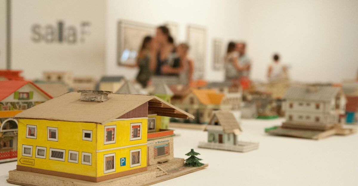 Detailed miniature house models displayed in an indoor exhibition setting with people in the background
