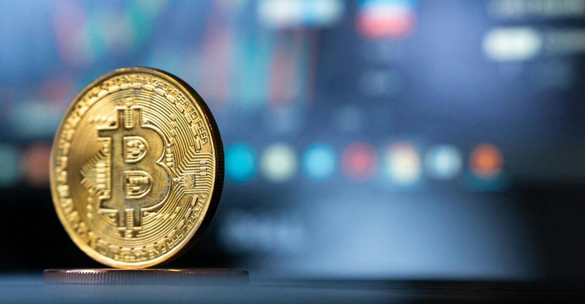 Gold Bitcoin coin with blurred financial chart in background representing cryptocurrency trading