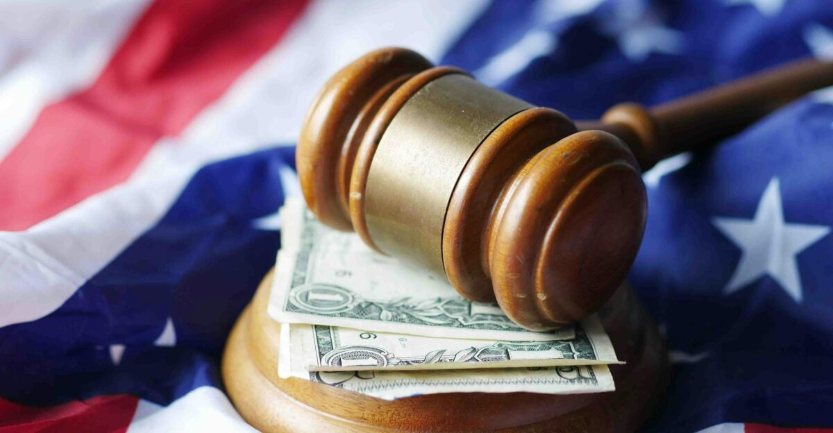 A gavel resting on dollar bills atop the American flag symbolizing justice and finance