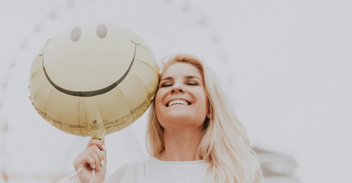 Cheerful woman holding a smiley balloon outdoors on a sunny day exuding happiness and positivity