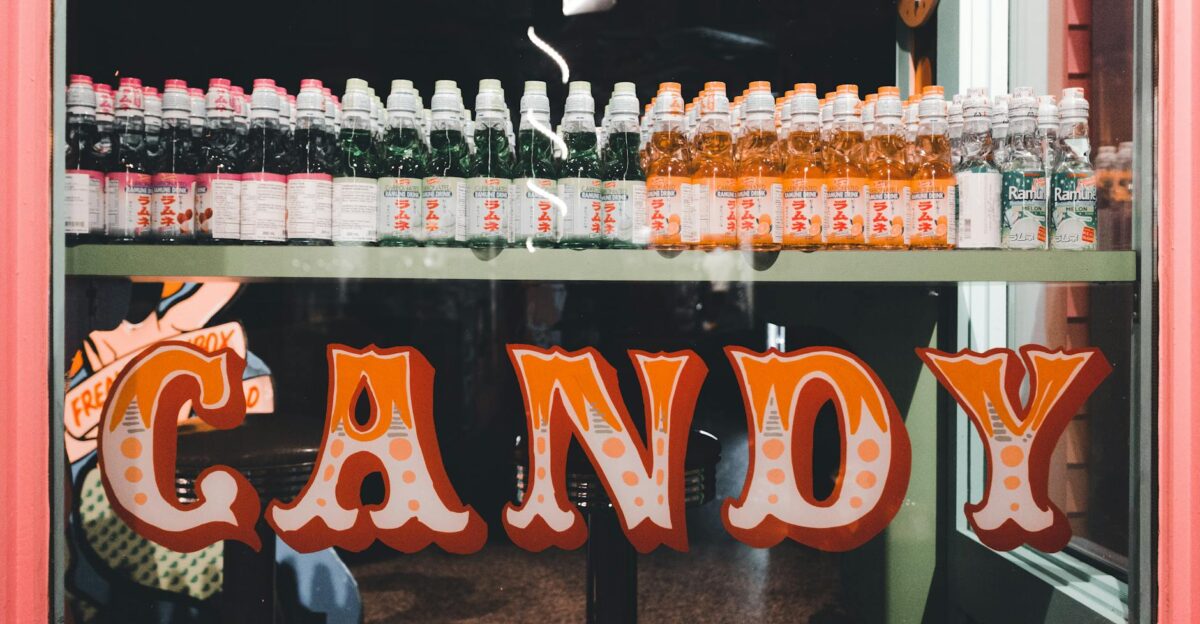 An array of colorful beverage bottles showcased in a vintage-style candy shop window