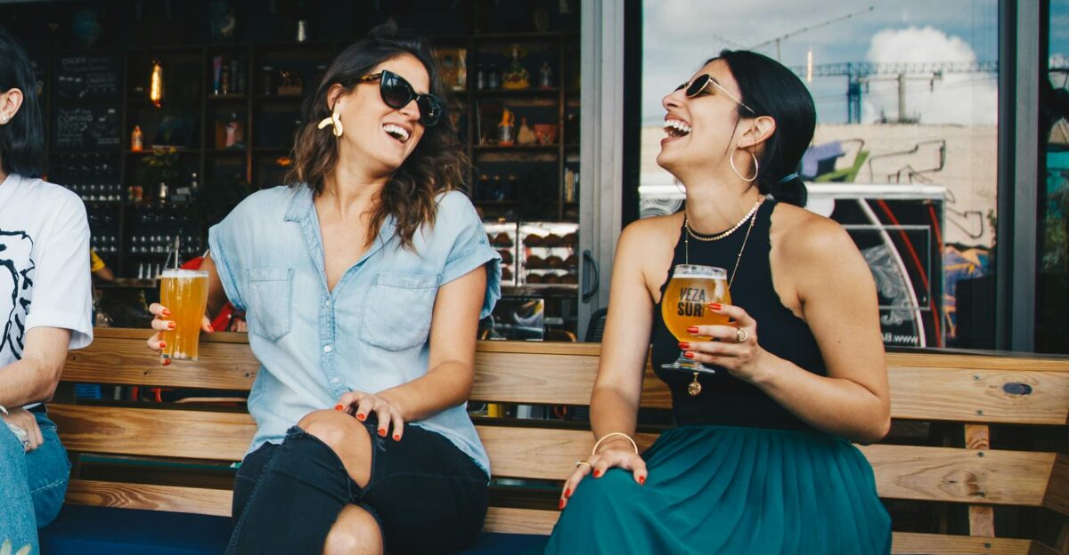 Two women laughing and enjoying drinks outdoors at a trendy bar creating a vibrant and social atmosphere