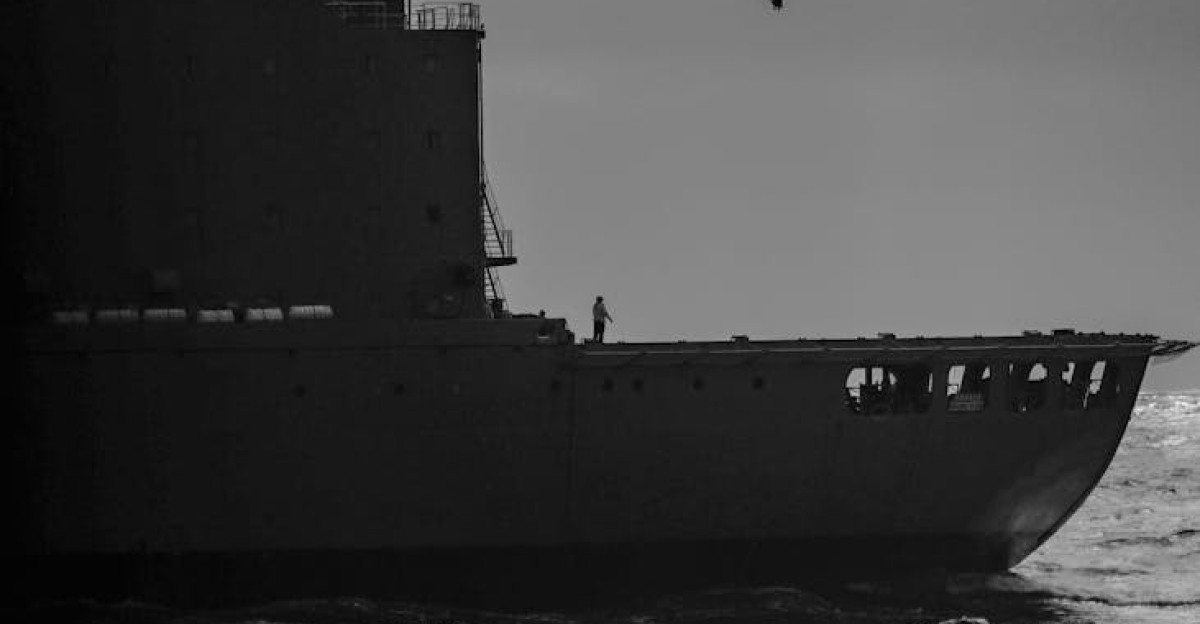 Dramatic black and white image of a military helicopter flying over a naval warship on the ocean