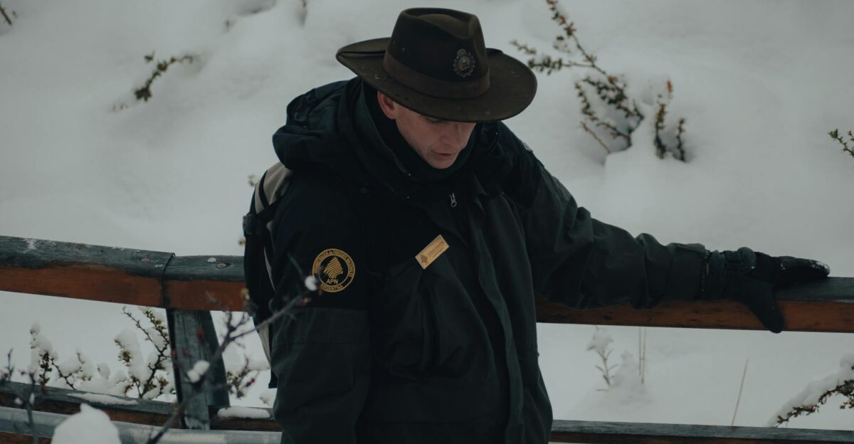 A park ranger in winter attire stands on a snow-covered bridge reflecting tranquility in nature
