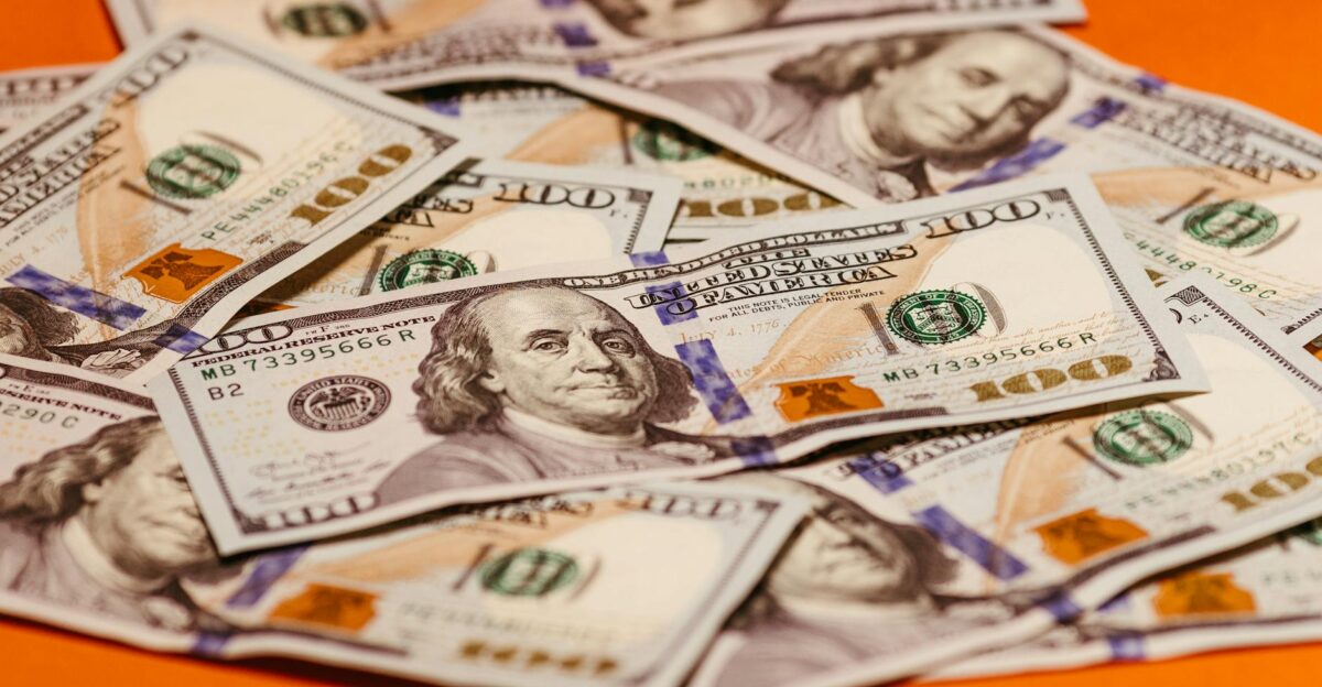 Scattered US 100 bills on a vibrant orange surface symbolizing wealth and finance