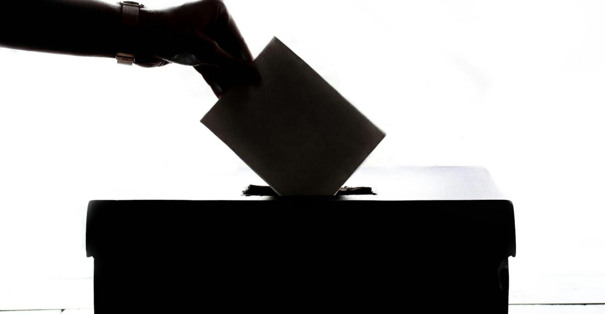 Silhouette of a hand placing a vote into a ballot box symbolizing democracy