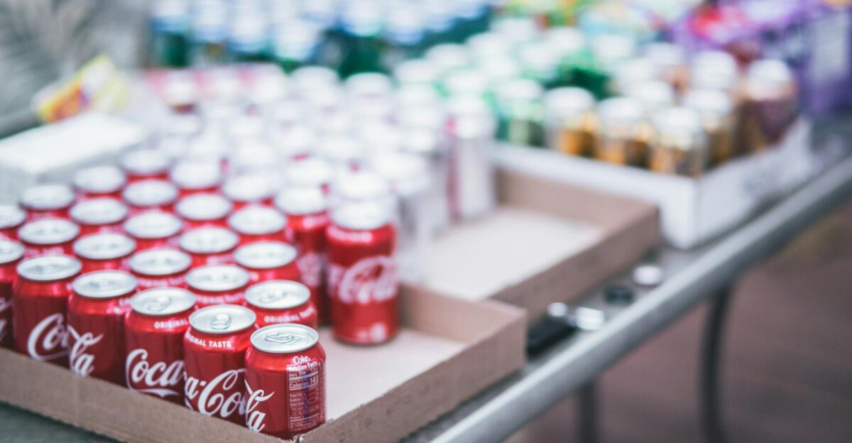 Blurred image of assorted beverage cans on a table featuring Coca-Cola