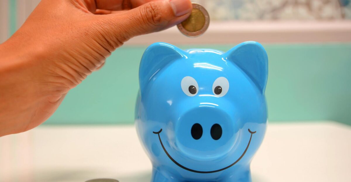 Hand inserting a coin into a blue piggy bank for savings and money management