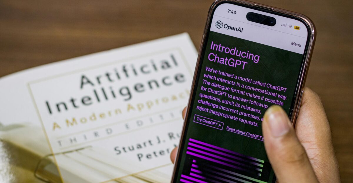 Close-up of a smartphone displaying ChatGPT app held over AI textbook