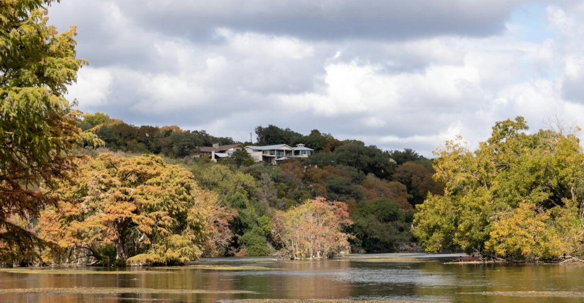 A serene autumn landscape of trees and a house by a lake in New Braunfels Texas