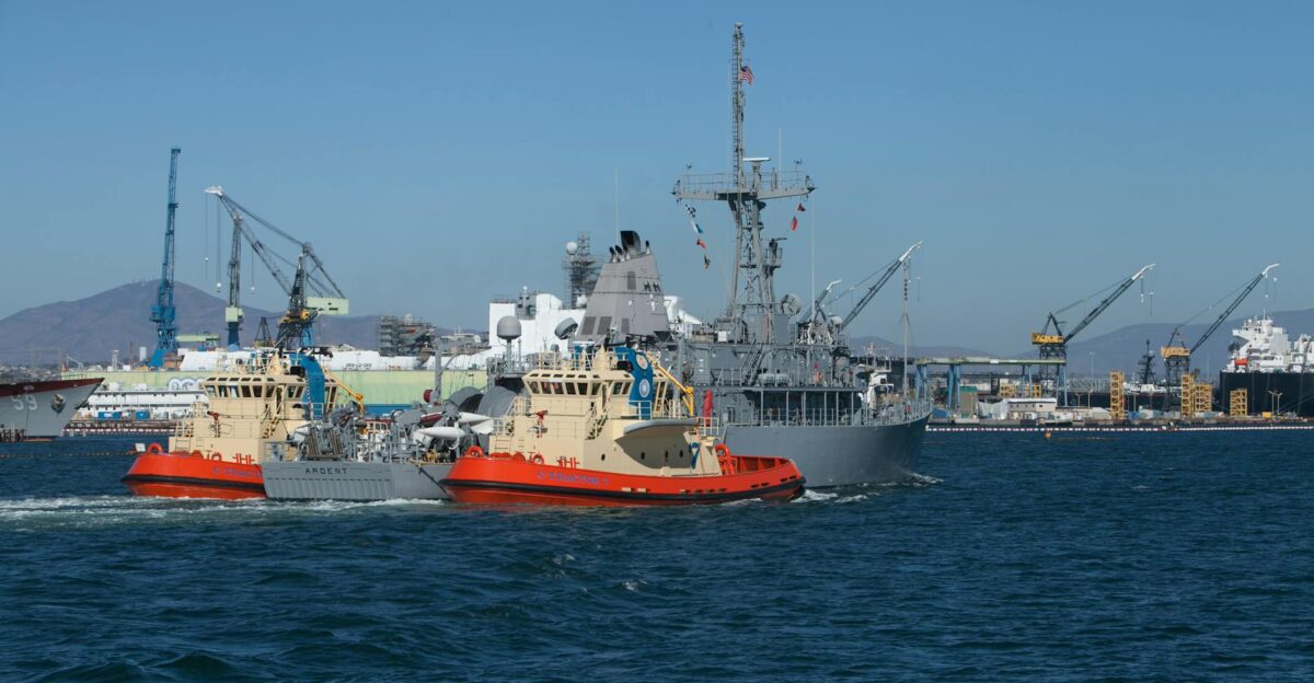 Navy vessel accompanied by tugboats in San Francisco harbor showcasing marine industry activity