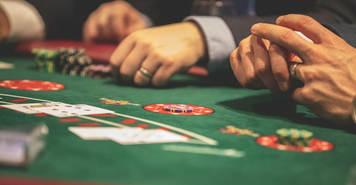 Hands playing blackjack in a casino setting with cards and chips on a green table