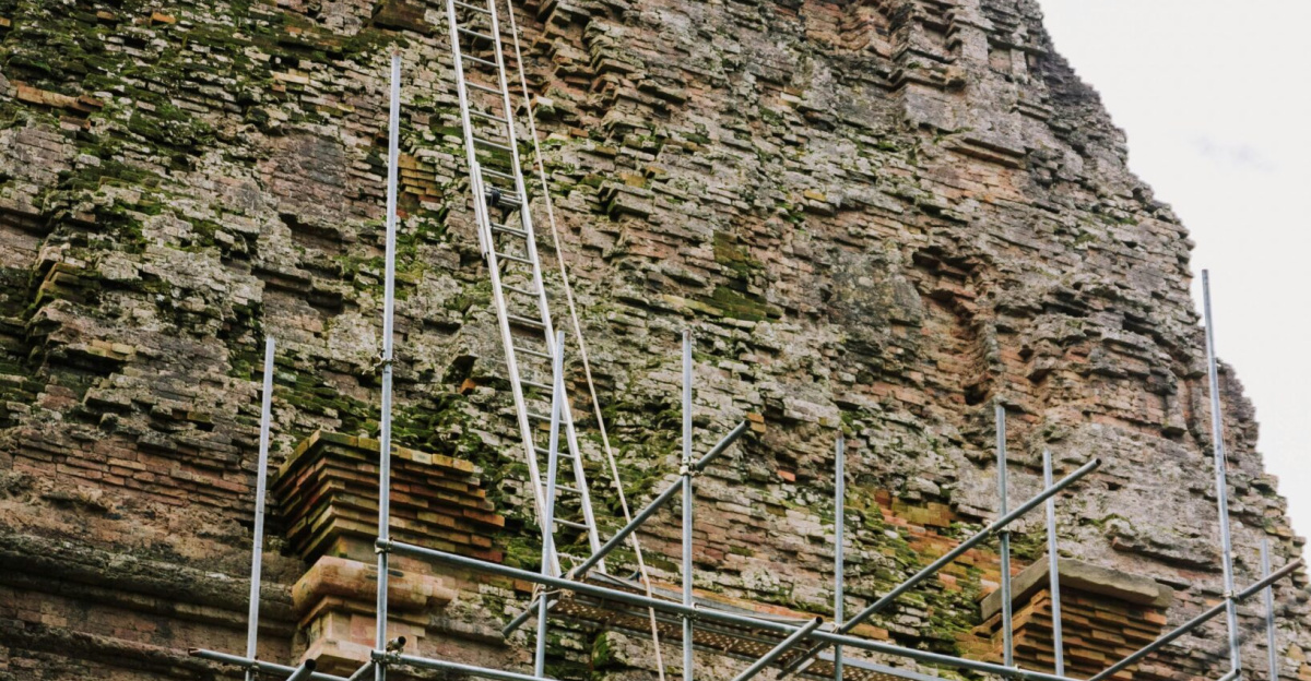 A temple wall undergoing restoration with scaffolding under a cloudy sky.