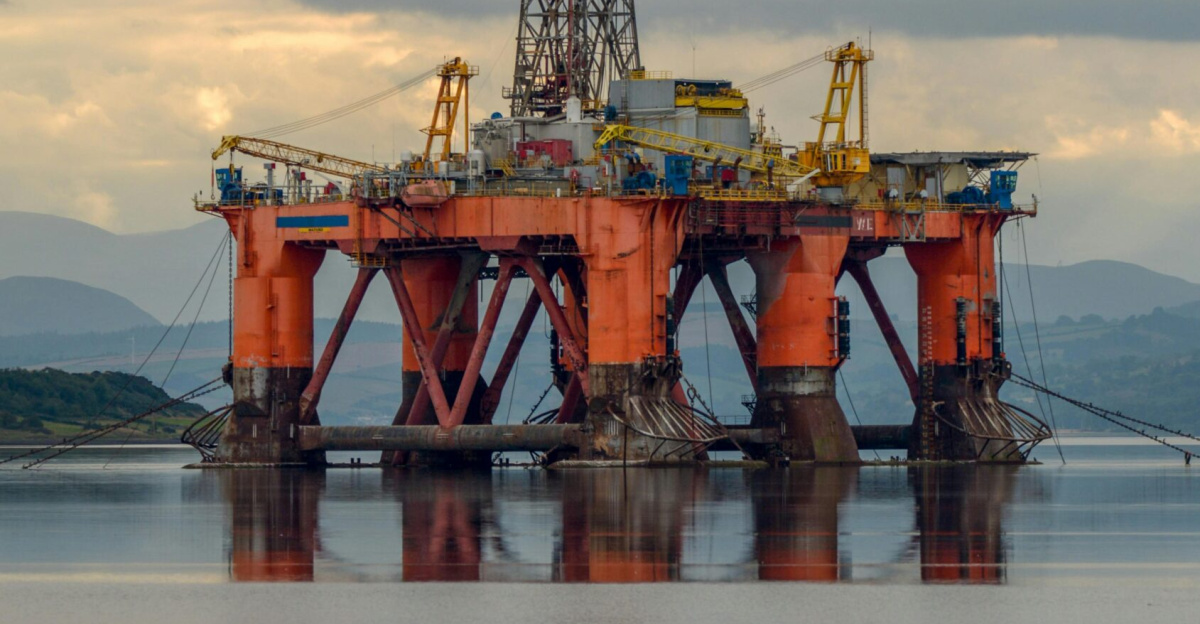 A large offshore oil rig reflects in calm waters under a cloudy sky, United Kingdom.