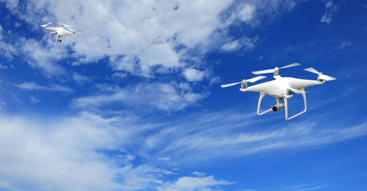 A stunning capture of two drones flying against a bright blue sky with soft clouds