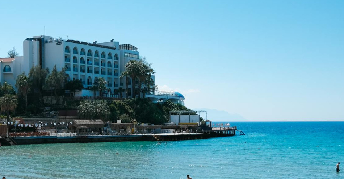 People enjoying a sunny day at a Mediterranean beach with clear blue waters and beachfront hotels