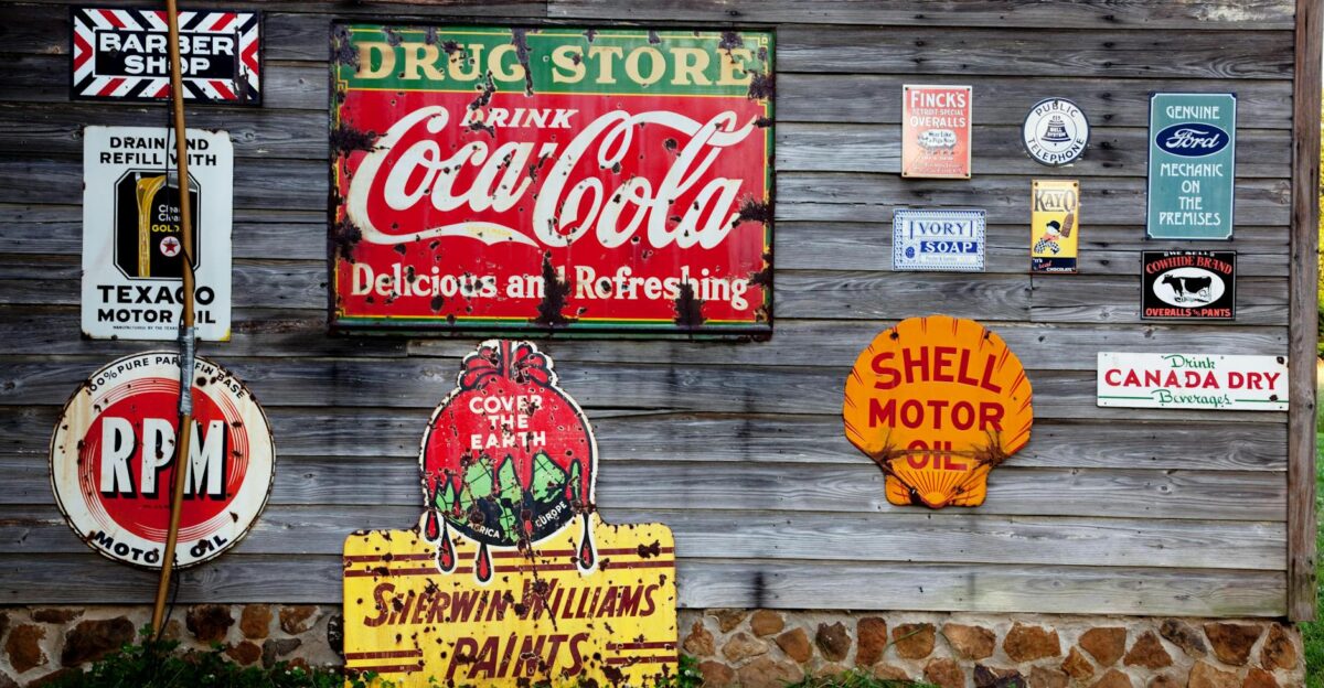 Collection of vintage advertising signs on rustic wooden wall showcasing classic brands