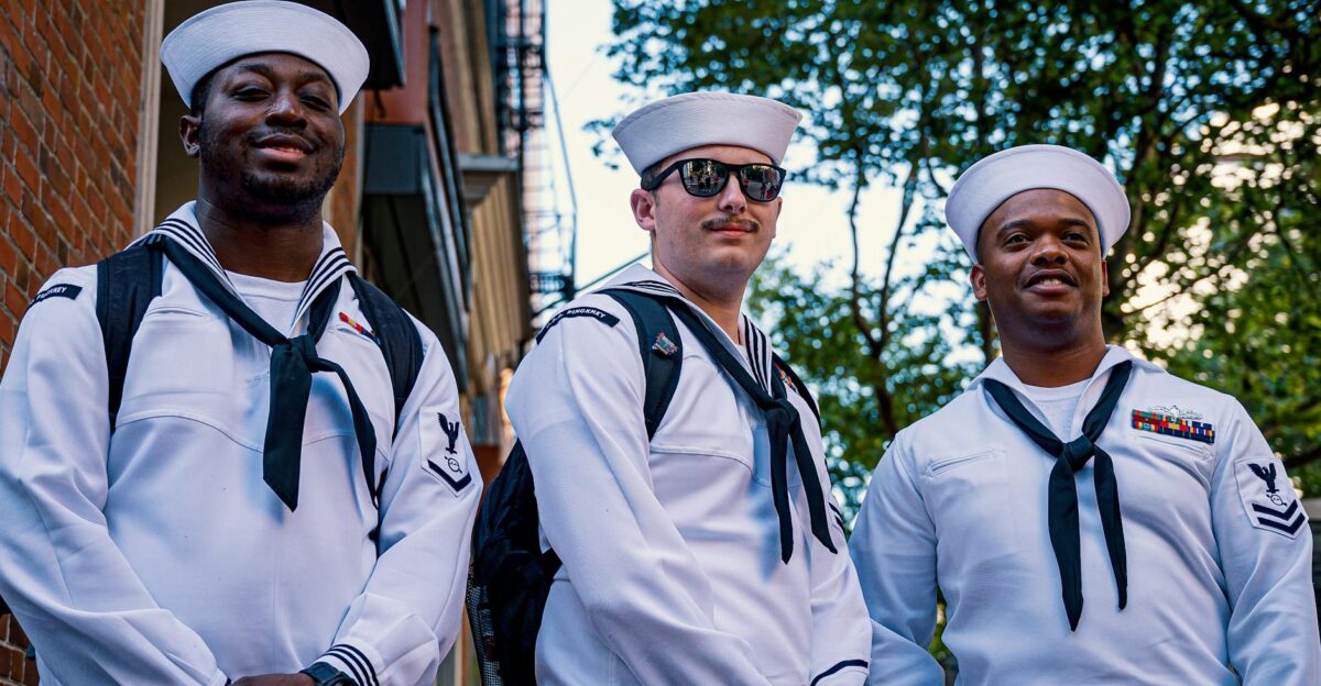 Three navy sailors pose outdoors in uniform showcasing diversity and camaraderie