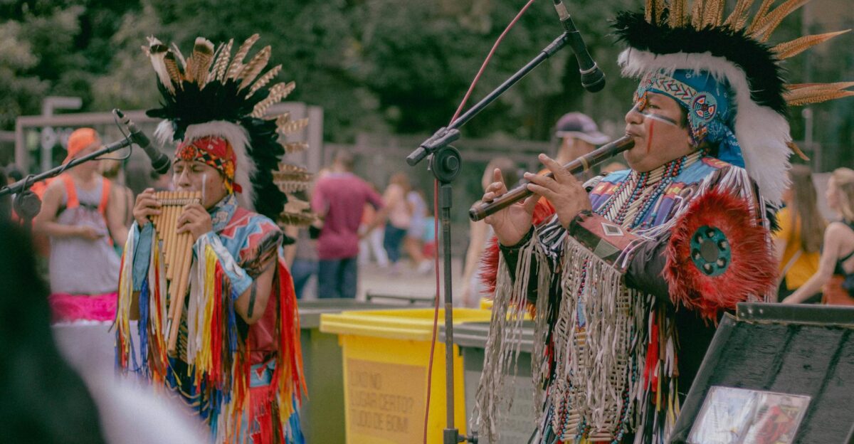 Native American musicians performing outdoors in traditional wear with woodwind instruments