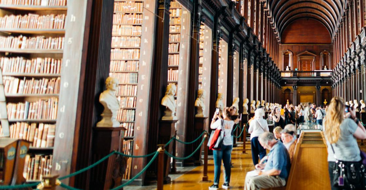 Visitors explore a grand library hallway with towering bookshelves in an iconic university