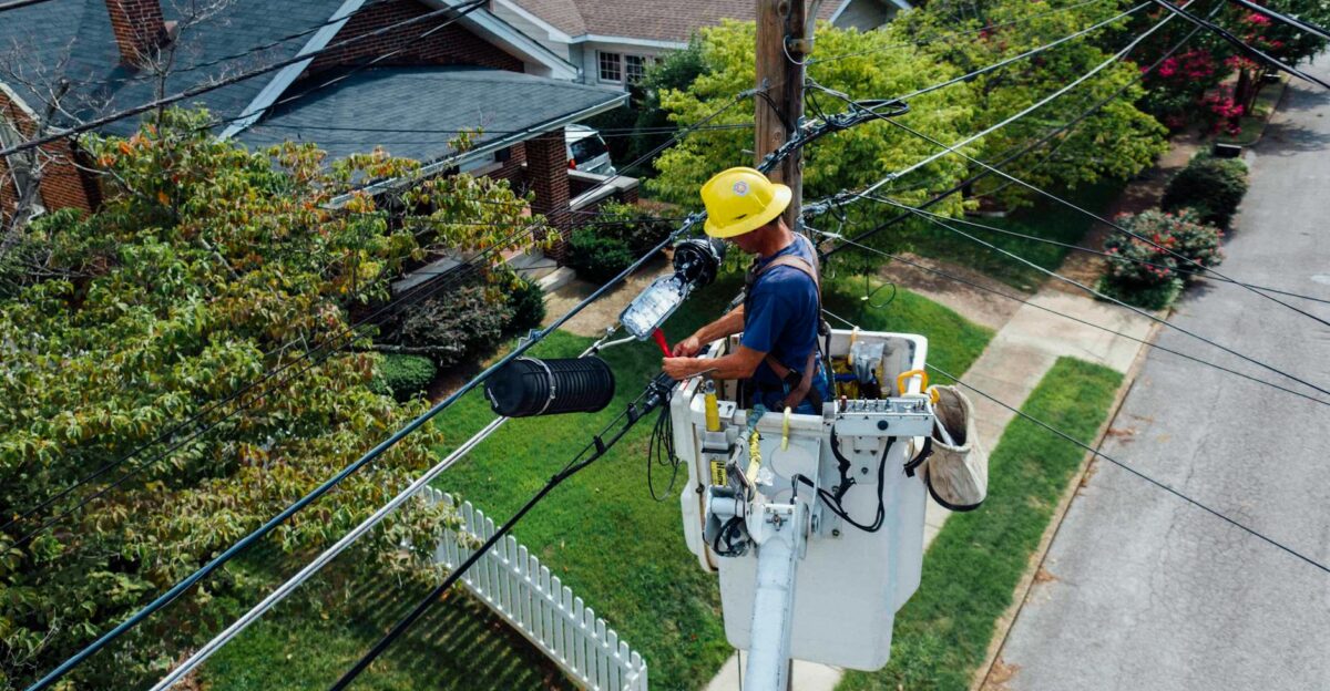Electrician in a bucket lift repairing power lines from a utility pole in a suburban neighborhood