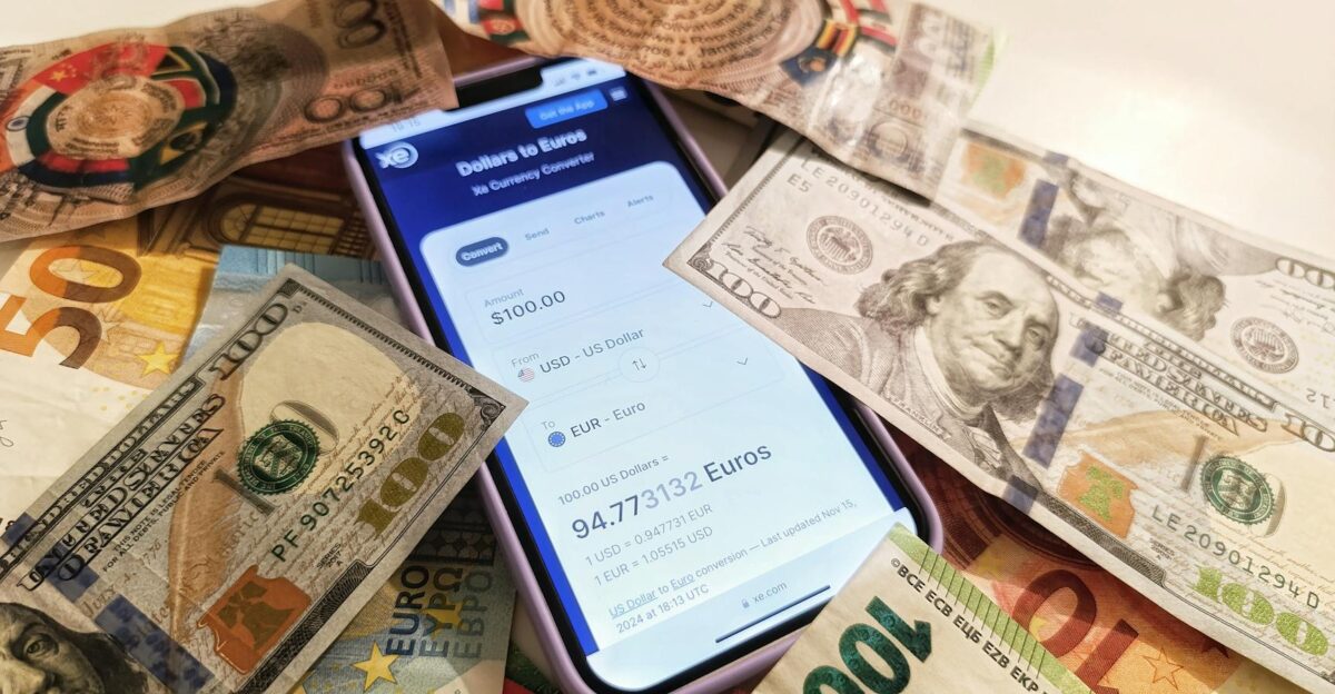A smartphone displaying a currency converter surrounded by dollar and euro banknotes highlighting exchange rates