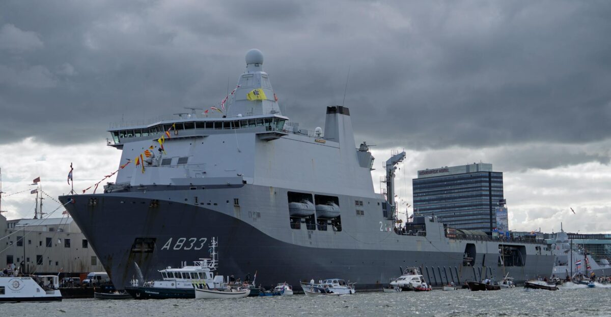 A large navy ship A833 docked in a busy harbor with smaller boats and cloudy skies
