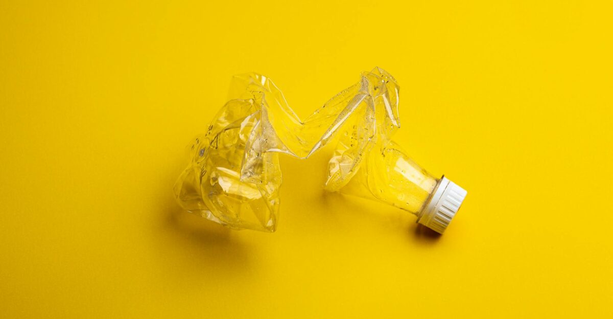 A crumpled plastic bottle against a bright yellow backdrop highlighting recycling themes
