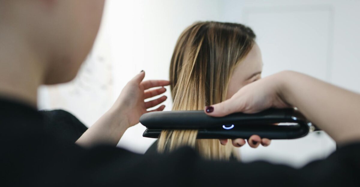 Close-up of a hairstylist using a straightening iron for sleek hairstyle indoors