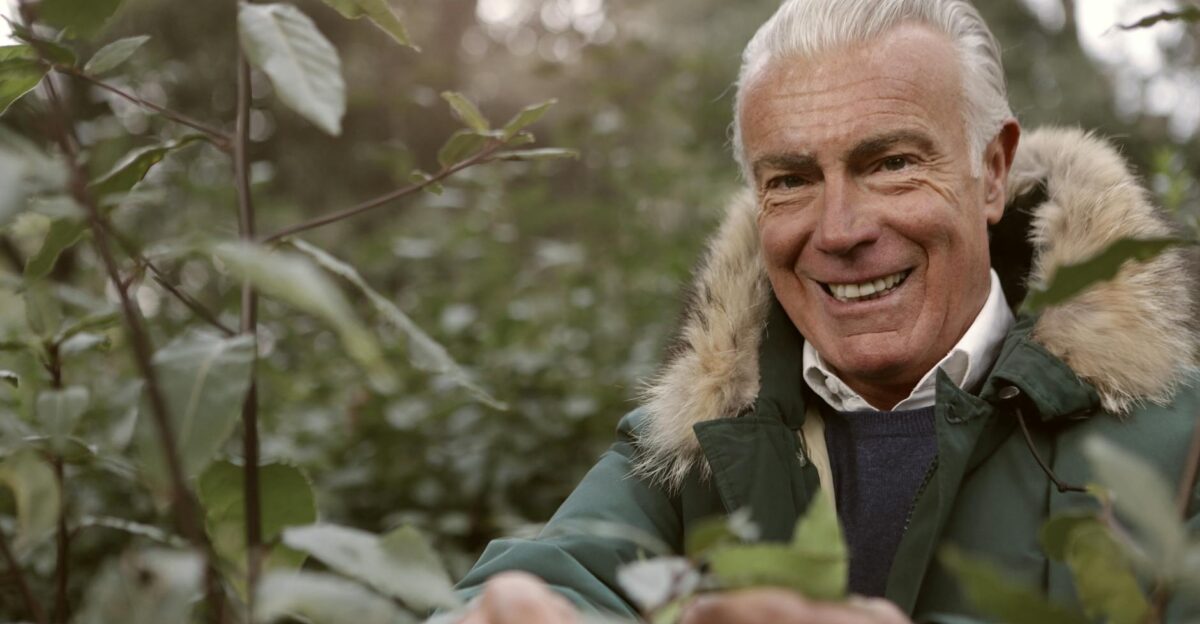 A smiling senior man in a green parka explores the autumn forest enjoying the outdoors
