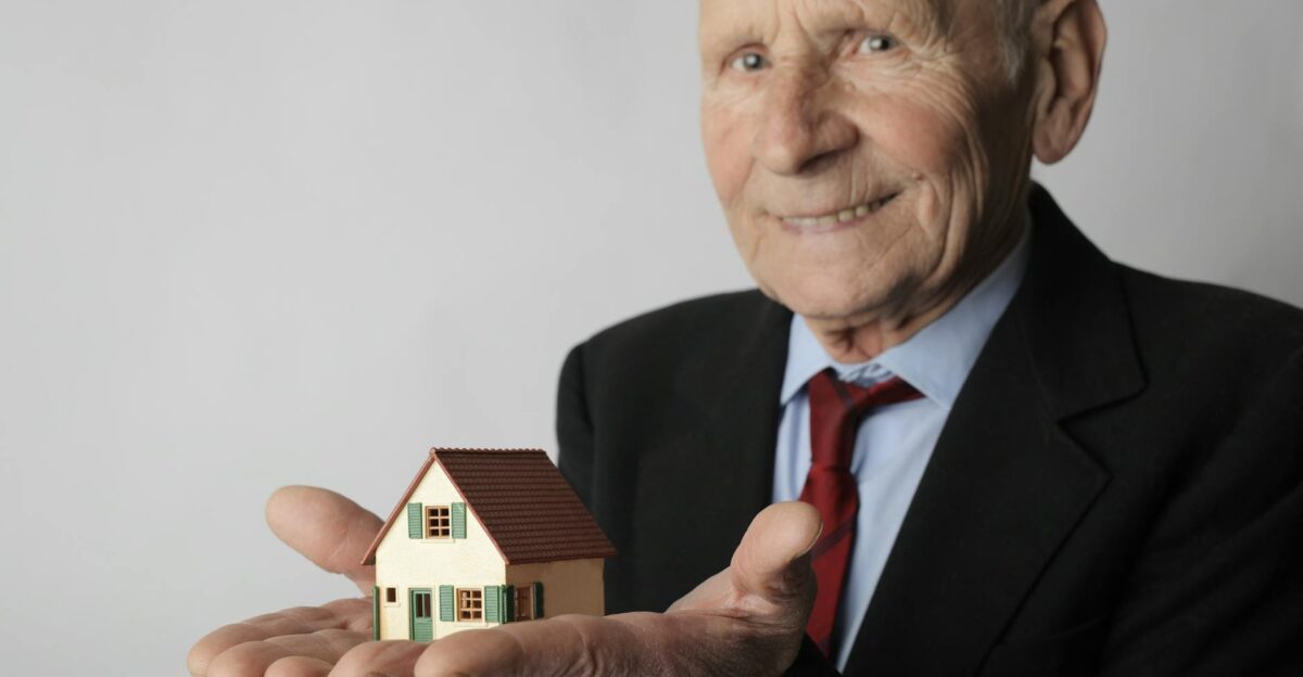 Elderly man in business attire holding a small house model symbolizing real estate investment