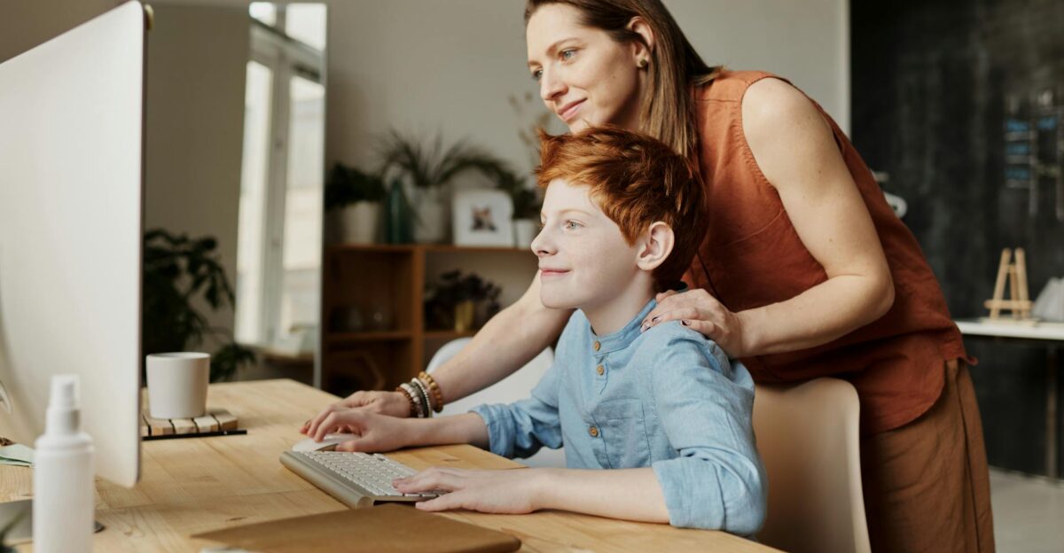 A mother and her child smiling while using a computer at home focused on learning