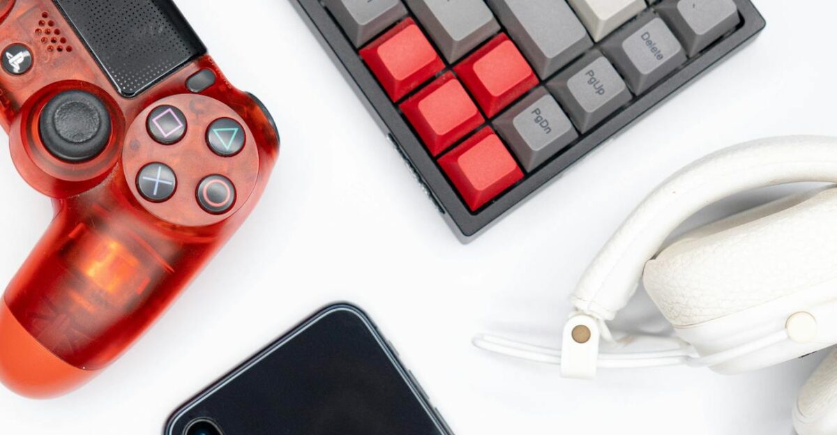 Top view of modern tech gadgets including gaming controller smartphone keyboard and headphones