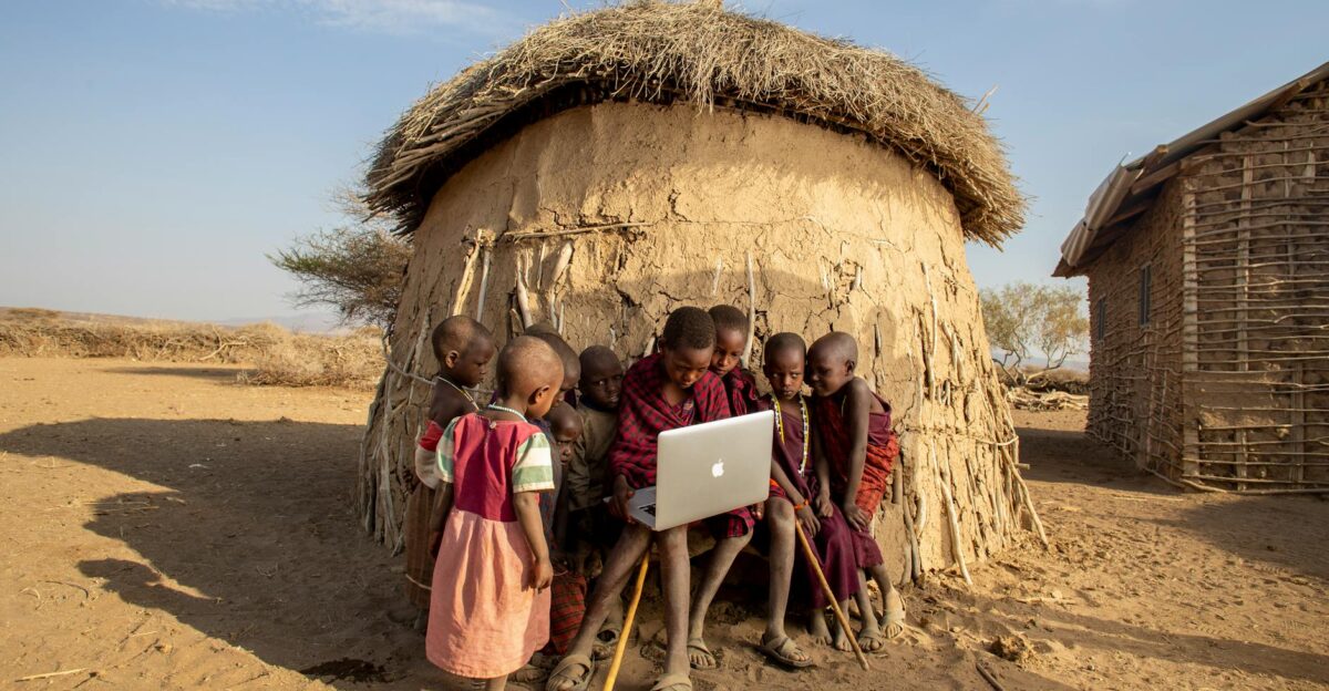 Group of African children in a Tanzanian village using a laptop outdoors engaged in learning