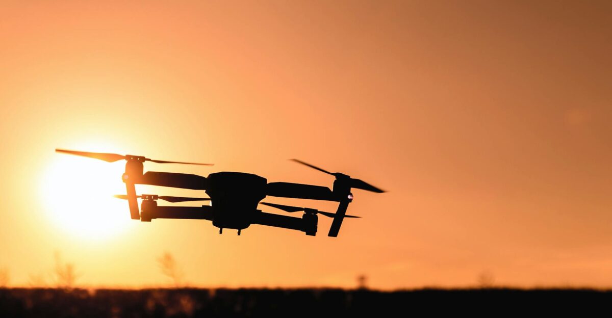 A drone in silhouette against a vibrant orange sunset sky showcasing modern technology and aerial photography