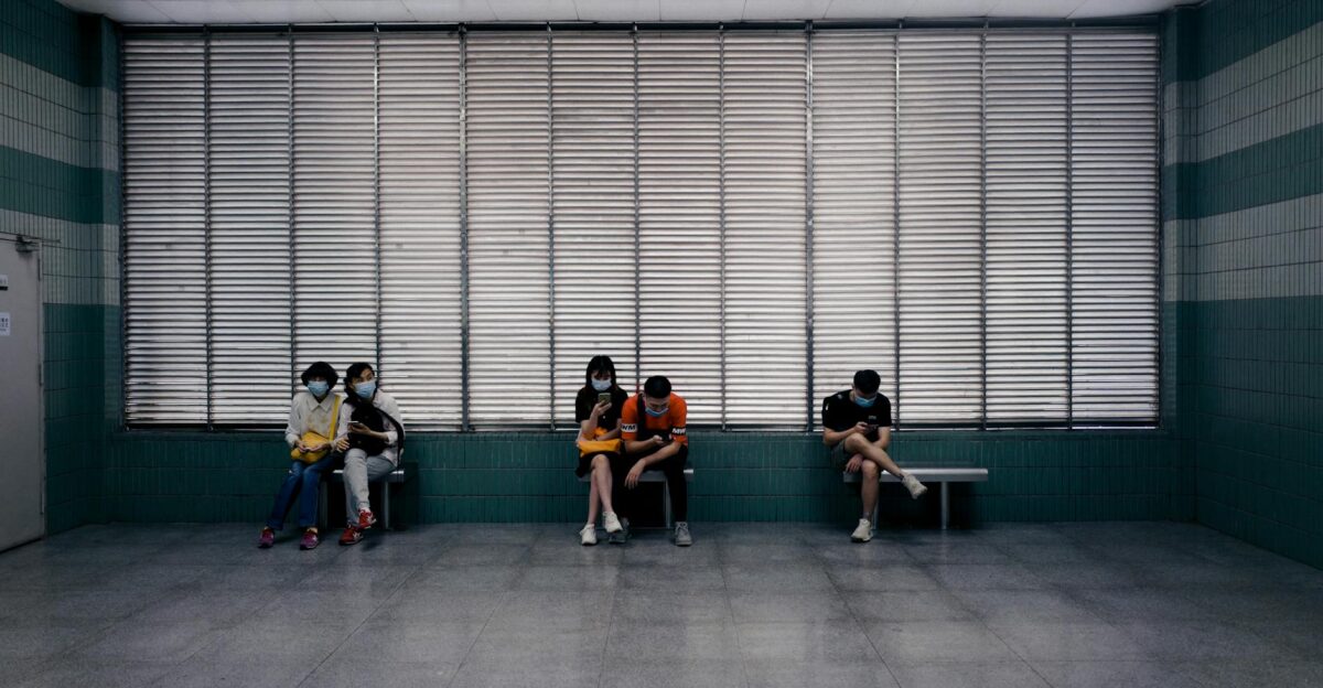 Individuals seated in a hospital lobby wearing masks following pandemic guidelines