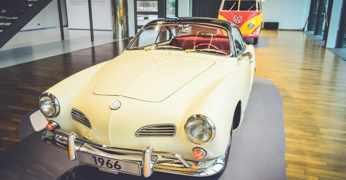 Vintage 1966 Volkswagen on display indoors with Kombi van in background