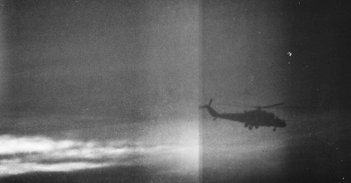 Atmospheric black and white photo of a military helicopter silhouette against a dramatic cloudy sky