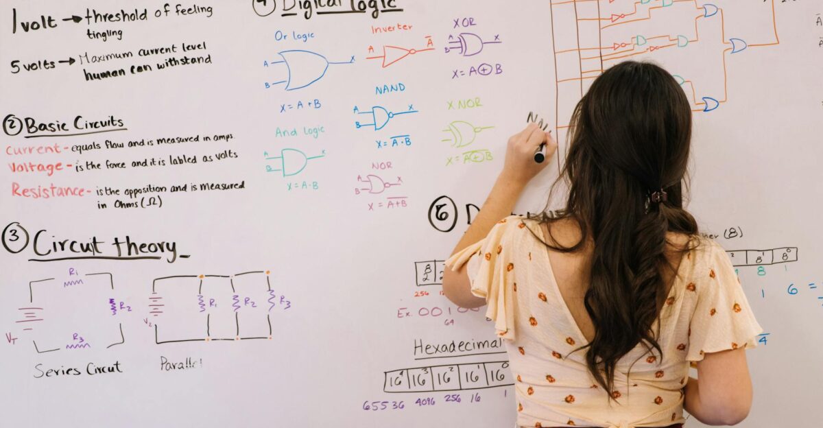Female student writing circuit diagrams and logic gates in an educational setting on a whiteboard