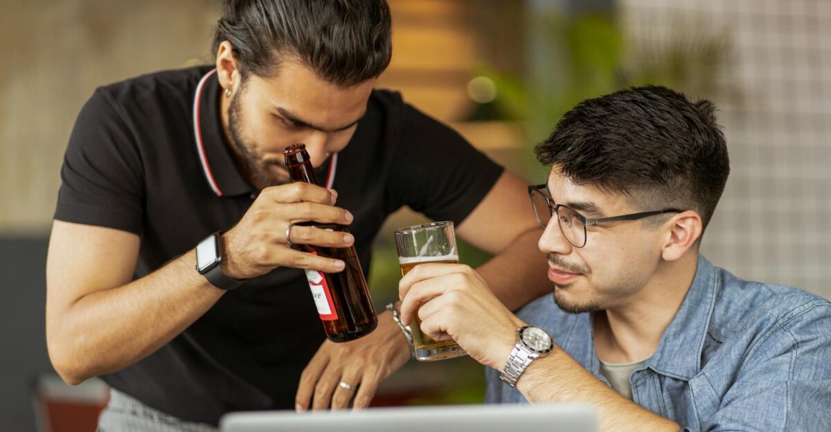 Two men casually enjoying drinks while collaborating on a project in an indoor setting