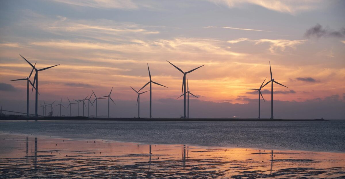 Wind turbines on the shoreline silhouette against a vibrant sunset promoting renewable energy