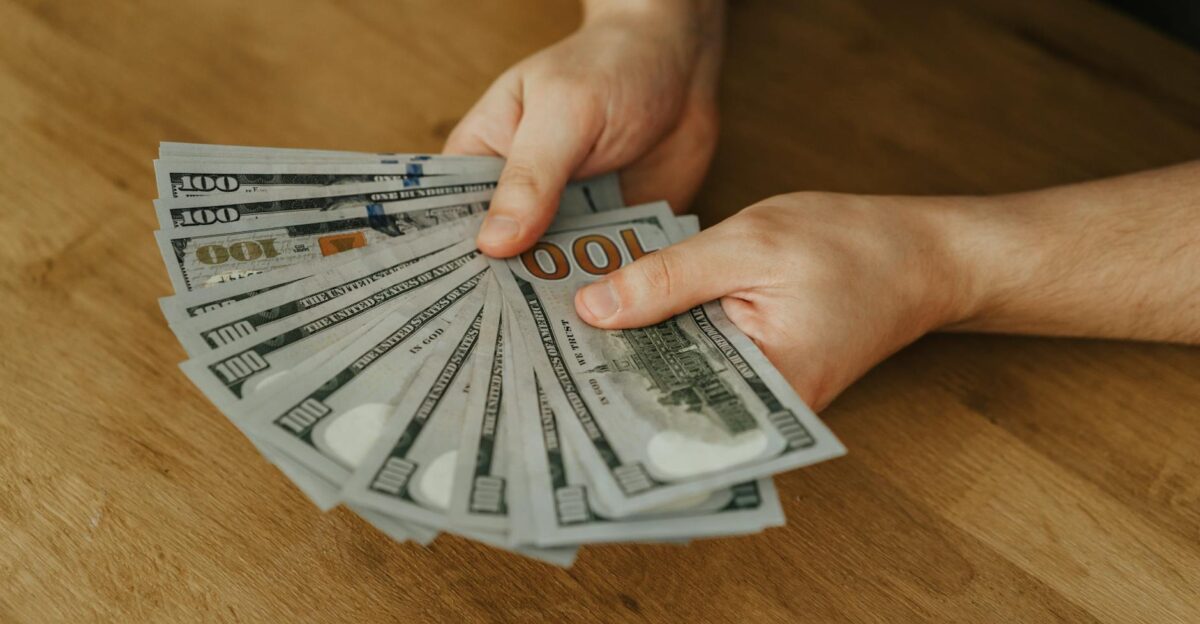 Close-up of hands holding several 100 US dollar bills on a wooden surface