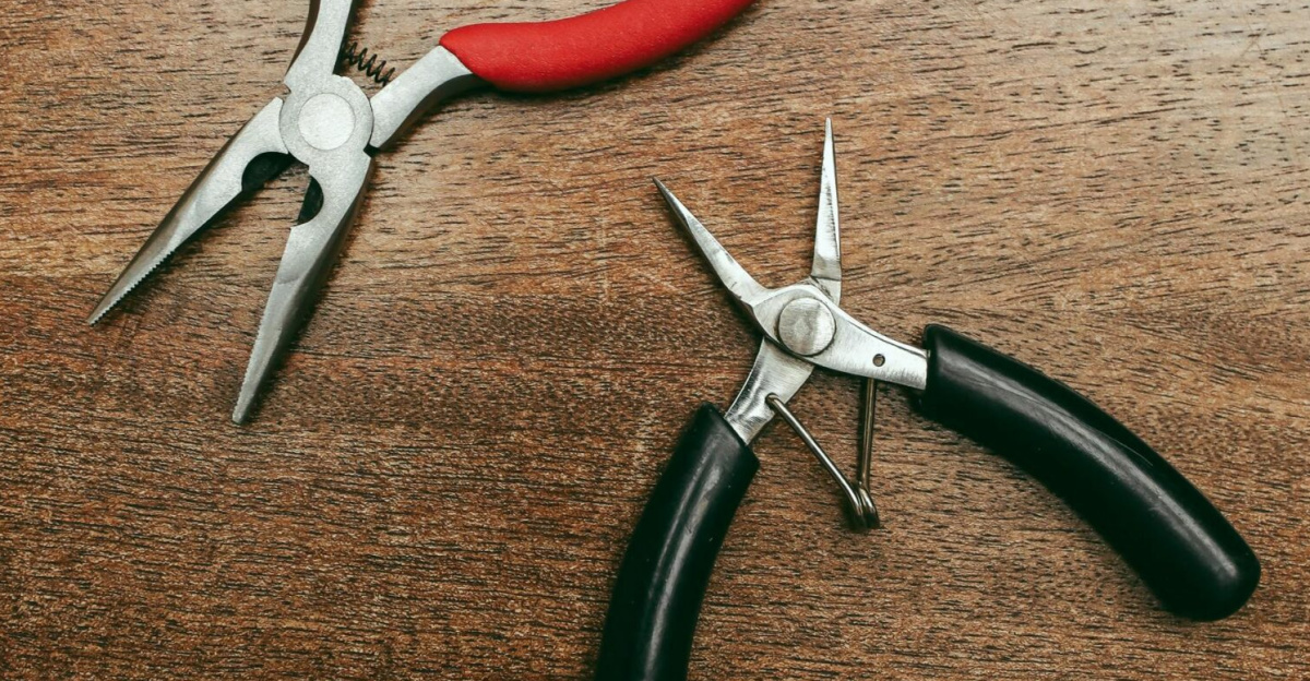 Two pliers with red and black handles on a wooden background.