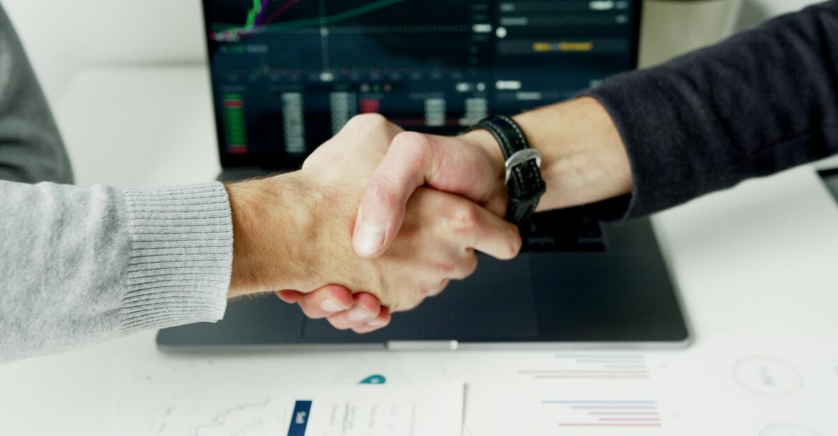 Close-up of a handshake with financial graphs on laptop screen symbolizing a successful agreement