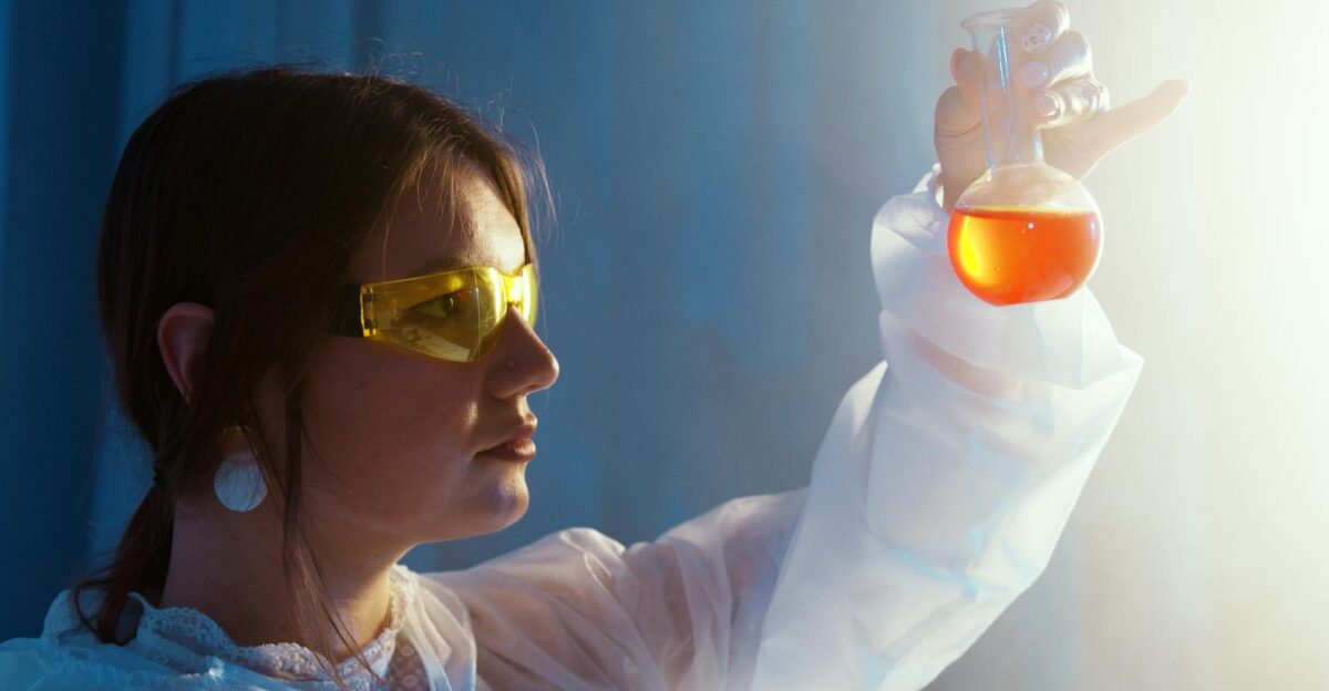 Woman in lab coat examining a vibrant liquid in a flask under lab lights