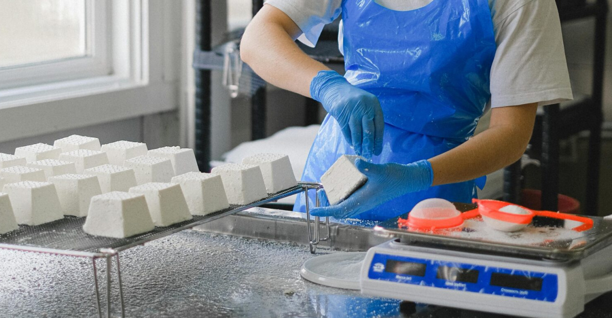 A factory worker in protective clothing packages sugar cubes inside an industrial setting.
