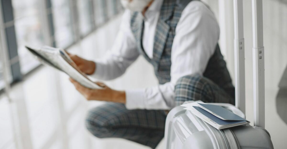 Adult man in plaid suit reads newspaper with suitcase at airport terminal