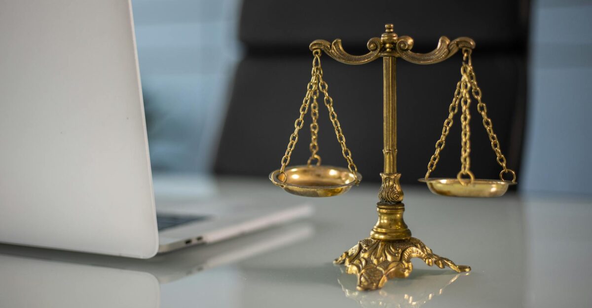 Golden justice scales on a desk beside a laptop symbolizing law and balance