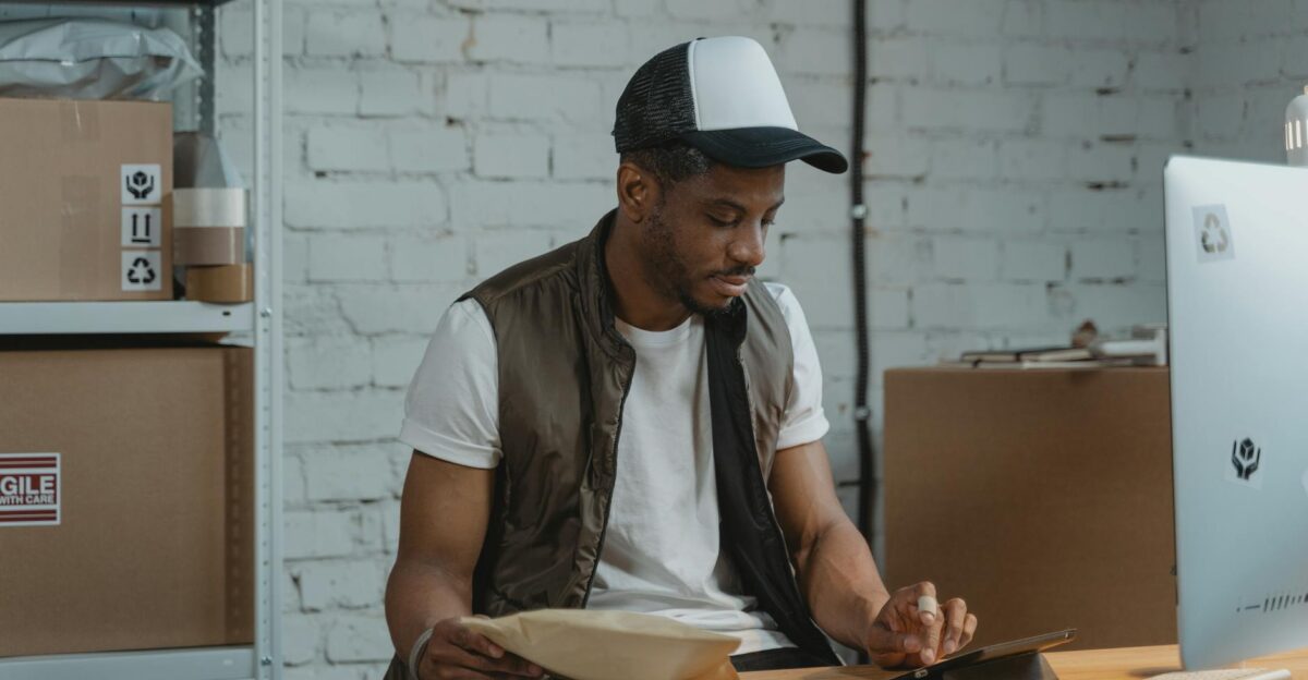A man in a warehouse managing e-commerce orders and using a tablet for logistics